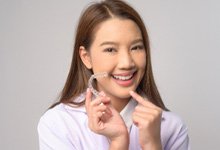 Smiling patient pointing to Invisalign aligner 