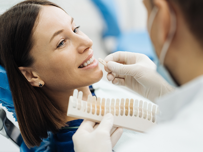 Dentist holding veneers in front of a patient's smile
