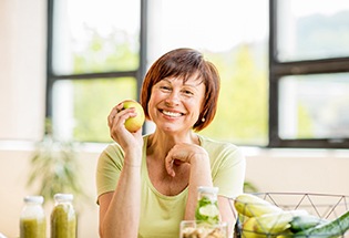 smiling woman with dental implants in San Antonio holding an apple 