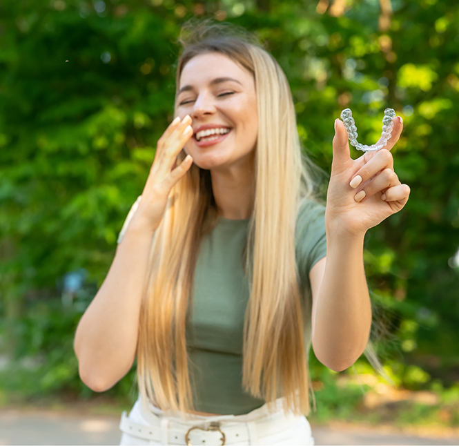 Smiling blonde woman holding Invisalign in San Antonio