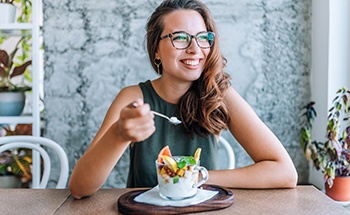 Woman with glasses smiling while eating breakfast